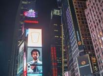 На фотографии изображён Таймс-сквер в Нью-Йорке, ярко освещённый неоновыми рекламами и огнями. Ночно