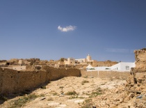 На фотографии изображены руины старинного города с каменными стенами и белыми домами на фоне ясного