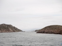 На фотографии изображен морской пейзаж с двумя скалистыми берегами, разделенными узким проливом. Вер