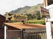 На фотографии изображена вывеска ресторана 'Antonio' в Перу, расположенного на фоне зеленых гор. Это