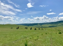 На фотографии изображено живописное ландшафтное пространство с зелеными холмами и каменными изваяния