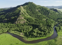На фотографии изображён живописный ландшафт с горой, окружённой зелеными лесами и извивающейся рекой