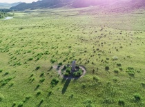 На фотографии изображен обширный зелёный ландшафт с одиноким каменным памятником в центре. Это место