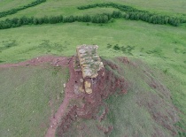 На фотографии изображен одинокий скальный выступ на фоне зелёных лугов и лесов. Это место, вероятно,
