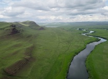 На фотографии изображены живописные зеленые холмы и извивающаяся река, окруженные обширными лугами.