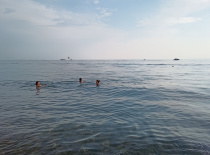 На фотографии видно троих человек, плавающих в спокойном море. Вода прозрачная, а на горизонте видны