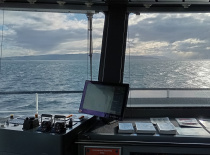 На фотографии вид из кабины судна, где видно море и облачное небо. На переднем плане расположены при