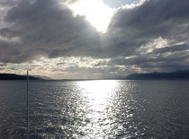 На фотографии изображено спокойное море с отражением солнечного света на воде. На горизонте видны го